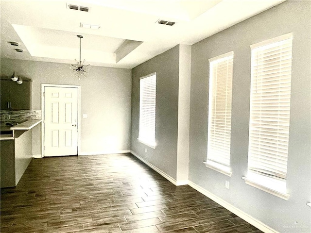 unfurnished dining area with a notable chandelier, dark hardwood / wood-style floors, and a tray ceiling