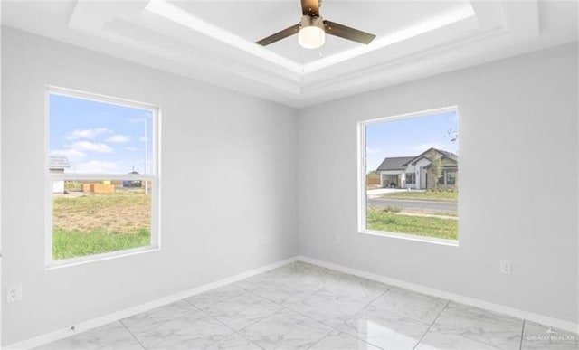 spare room featuring a tray ceiling, a wealth of natural light, and ceiling fan