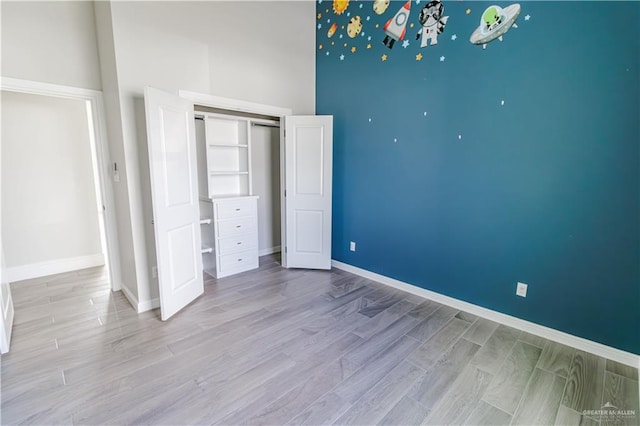 unfurnished bedroom featuring a high ceiling, light wood-type flooring, and a closet