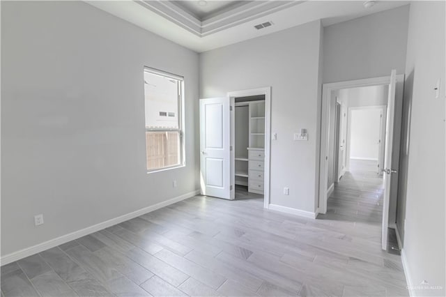 unfurnished bedroom featuring a raised ceiling and light wood-type flooring