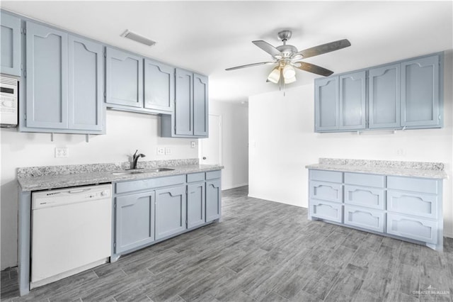 kitchen with a sink, visible vents, a ceiling fan, white appliances, and wood finished floors
