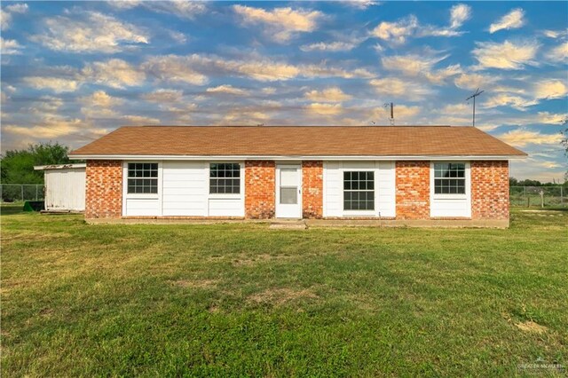 view of front facade with a lawn, fence, and brick siding