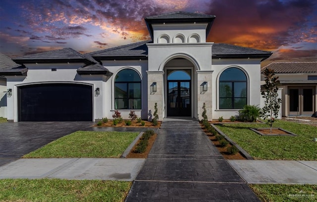 view of front of property featuring french doors, stucco siding, an attached garage, a front yard, and driveway