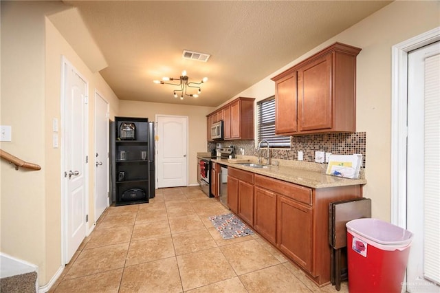 kitchen with sink, tasteful backsplash, light stone counters, light tile patterned floors, and appliances with stainless steel finishes