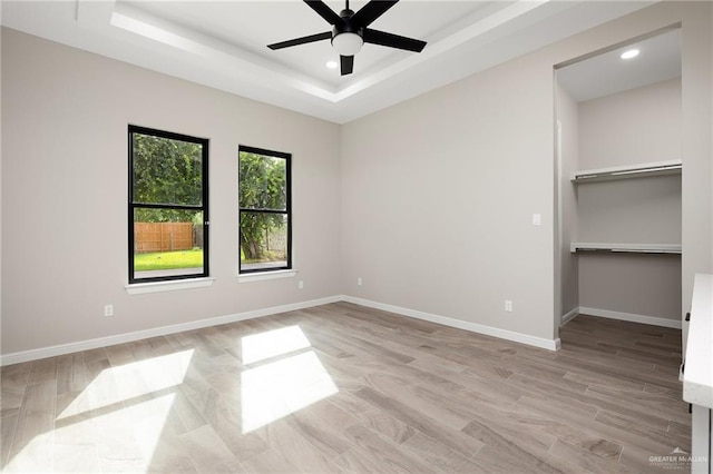 unfurnished bedroom featuring ceiling fan, a raised ceiling, and light hardwood / wood-style flooring