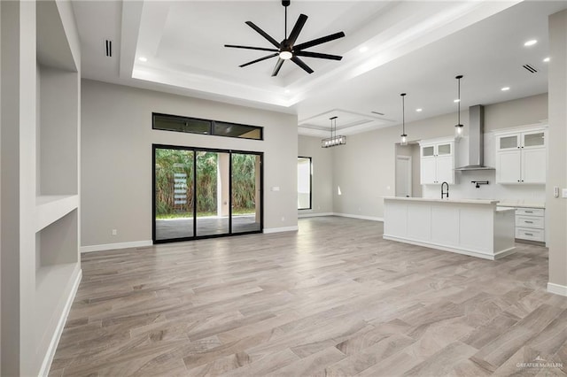 unfurnished living room with ceiling fan, light hardwood / wood-style floors, sink, and a tray ceiling