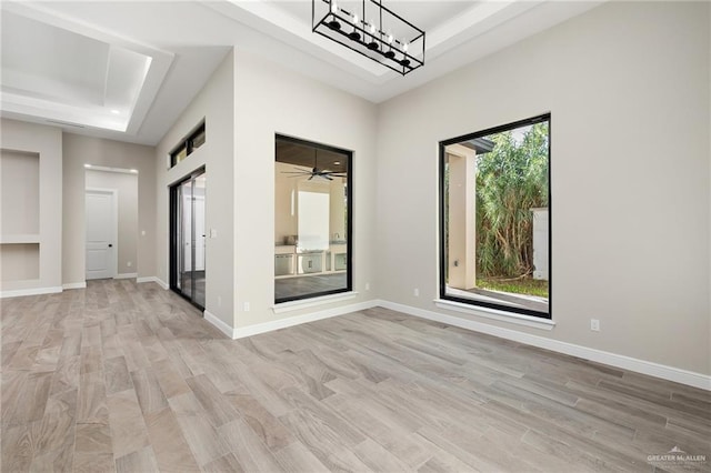 empty room featuring a raised ceiling, ceiling fan, light hardwood / wood-style flooring, and a healthy amount of sunlight