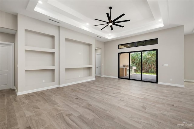 unfurnished living room with built in shelves, ceiling fan, light hardwood / wood-style flooring, and a tray ceiling