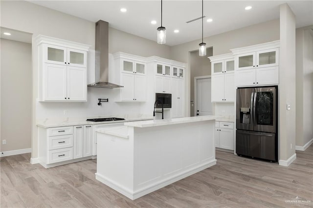 kitchen with white cabinets, wall chimney exhaust hood, stainless steel fridge, and an island with sink