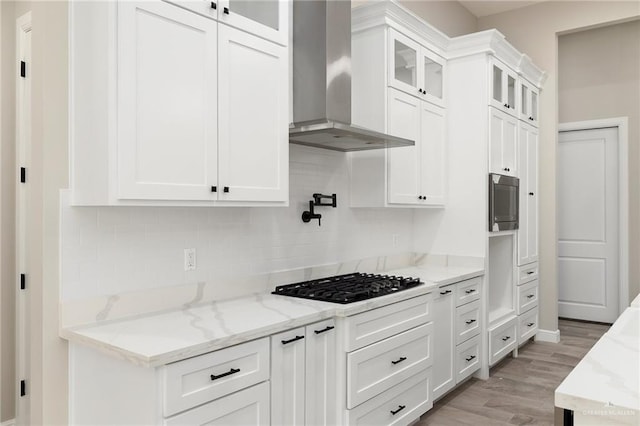 kitchen featuring light stone countertops, wall chimney exhaust hood, black gas cooktop, white cabinets, and light hardwood / wood-style floors