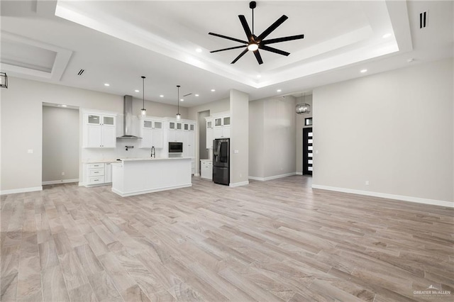 unfurnished living room featuring ceiling fan, light wood-type flooring, sink, and a tray ceiling