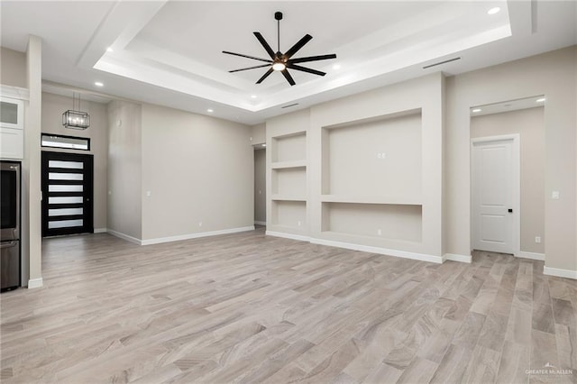 unfurnished living room featuring ceiling fan with notable chandelier, light hardwood / wood-style floors, and a tray ceiling