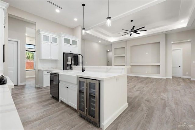 kitchen with a tray ceiling, a kitchen island with sink, pendant lighting, white cabinets, and wine cooler