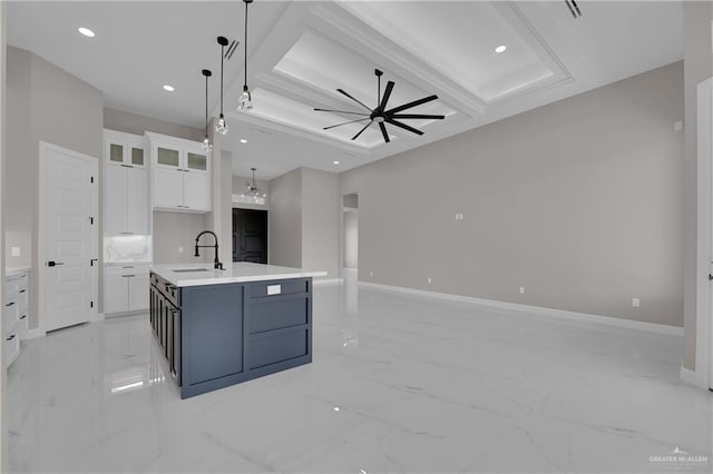 kitchen featuring white cabinetry, sink, ceiling fan, hanging light fixtures, and an island with sink