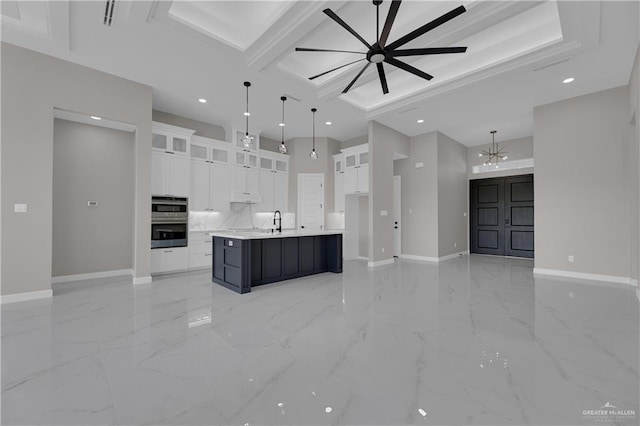 kitchen with decorative light fixtures, white cabinetry, sink, and a large island with sink