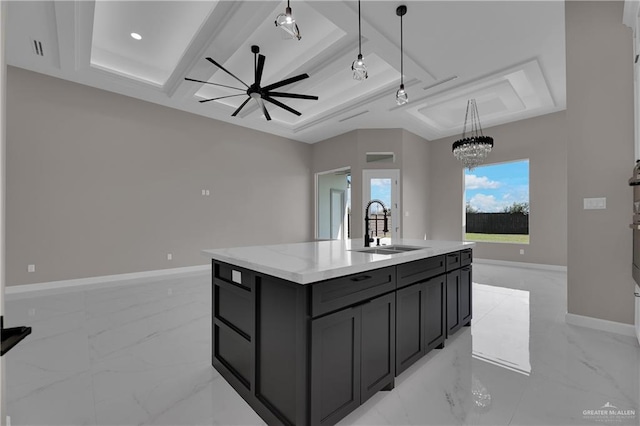 kitchen with sink, decorative light fixtures, a tray ceiling, a kitchen island with sink, and ceiling fan with notable chandelier