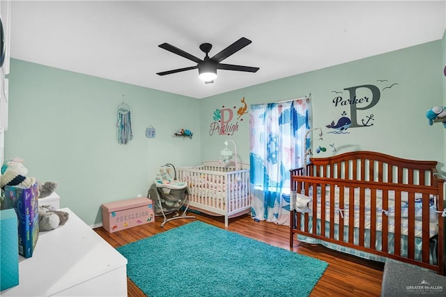 bedroom with a nursery area, ceiling fan, and dark wood-type flooring