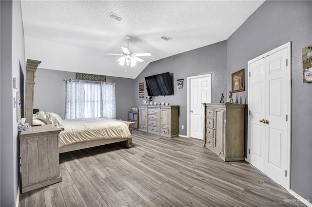 bedroom featuring a textured ceiling, light wood-type flooring, vaulted ceiling, and ceiling fan