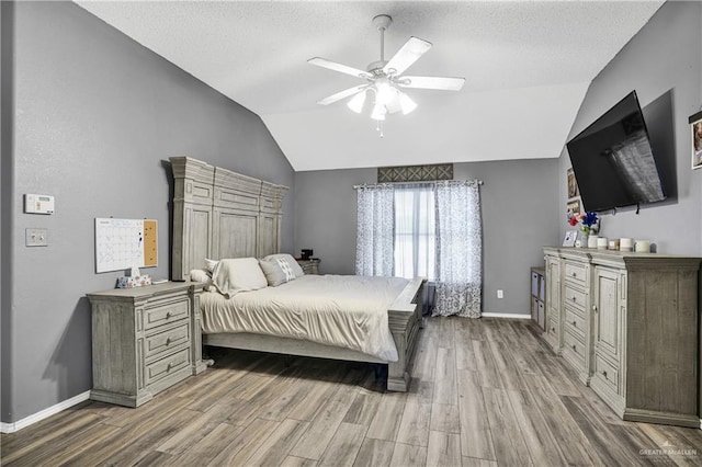 bedroom featuring a textured ceiling, light hardwood / wood-style flooring, vaulted ceiling, and ceiling fan