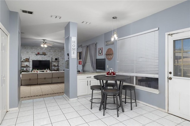 kitchen featuring white cabinetry, ceiling fan, hanging light fixtures, brick wall, and light tile patterned floors