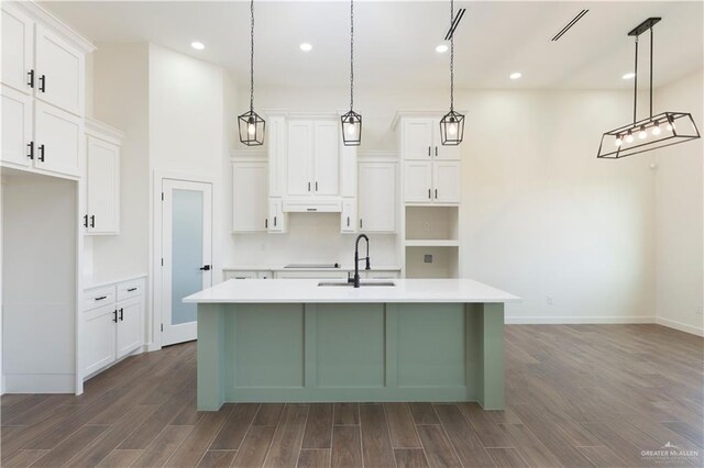 kitchen with a kitchen island with sink, a sink, white cabinetry, hanging light fixtures, and dark wood-style floors