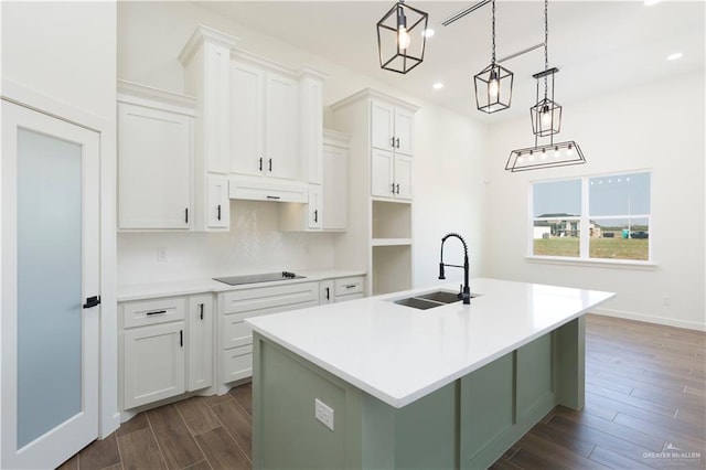 kitchen with dark wood-type flooring, a kitchen island with sink, under cabinet range hood, white cabinetry, and a sink