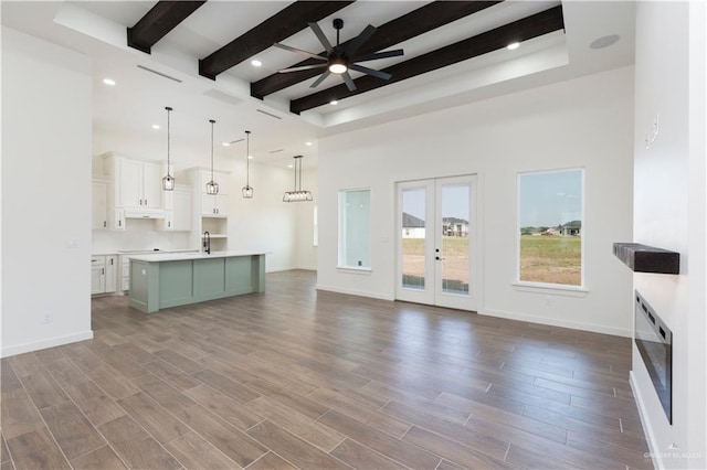 unfurnished living room featuring baseboards, a ceiling fan, wood finished floors, french doors, and beam ceiling