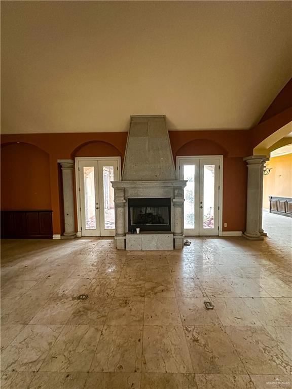 unfurnished living room with decorative columns, a fireplace, french doors, and high vaulted ceiling