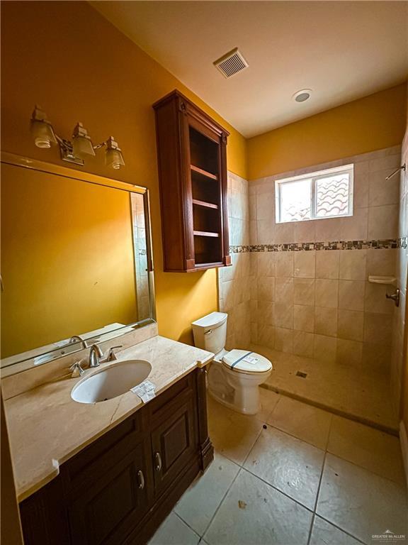 bathroom with tile patterned flooring, vanity, toilet, and a tile shower