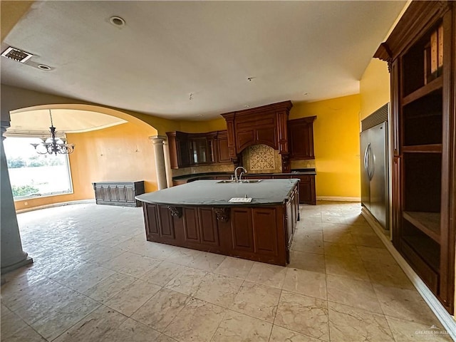 kitchen with a kitchen island with sink, sink, tasteful backsplash, a notable chandelier, and stainless steel built in refrigerator