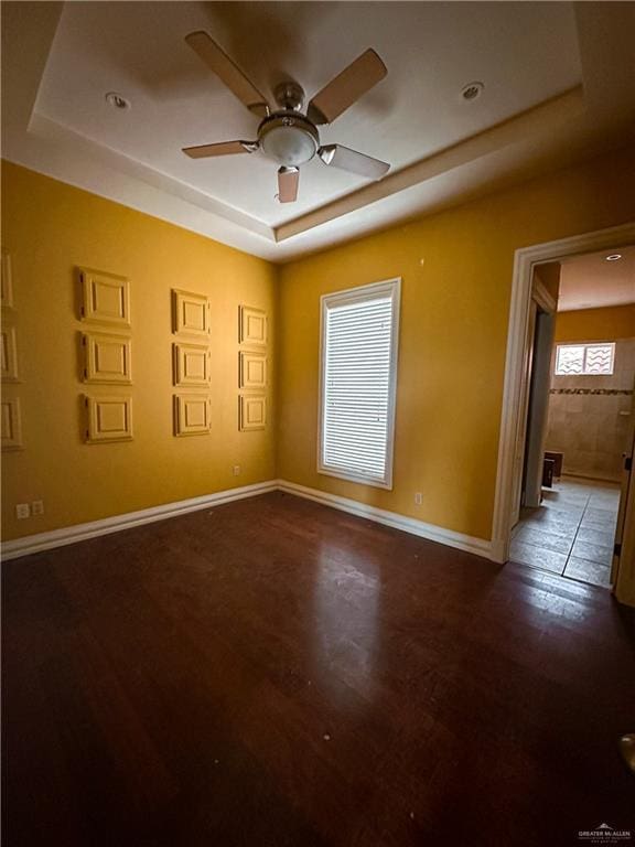 empty room with ceiling fan, dark wood-type flooring, and a tray ceiling