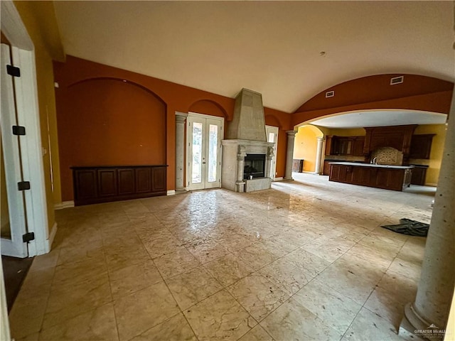 unfurnished living room with decorative columns, a fireplace, french doors, and lofted ceiling