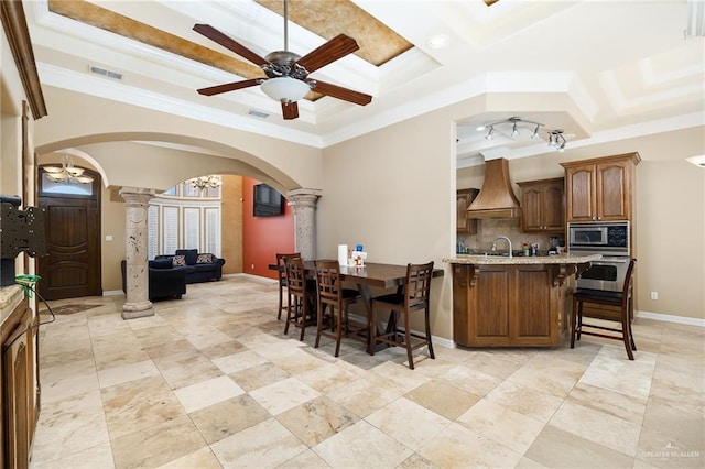 kitchen with wall chimney range hood, stainless steel appliances, a breakfast bar, and ornate columns