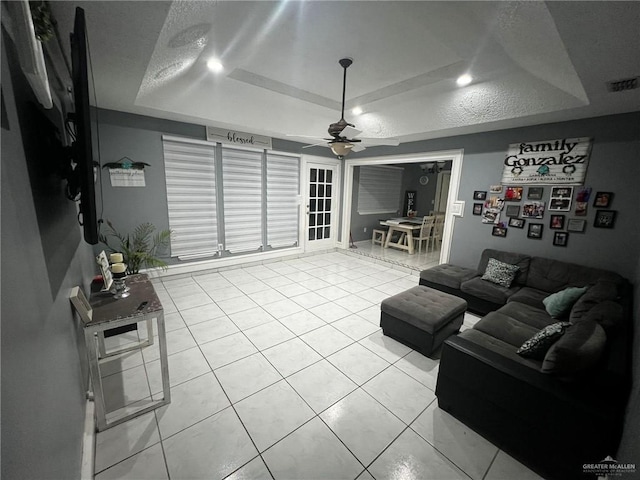 living room with ceiling fan, a raised ceiling, light tile patterned floors, and a textured ceiling