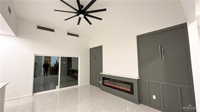 unfurnished living room featuring visible vents, a glass covered fireplace, a towering ceiling, ceiling fan, and a decorative wall