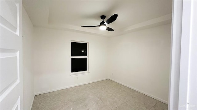 empty room featuring a tray ceiling, ceiling fan, and baseboards