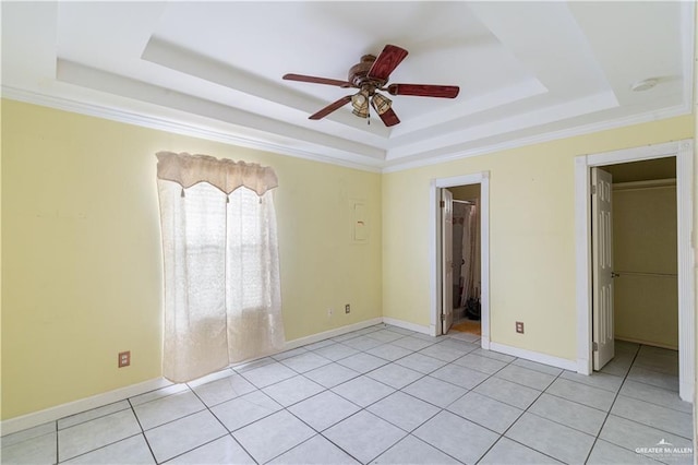 unfurnished bedroom featuring a walk in closet, light tile patterned floors, baseboards, and a raised ceiling