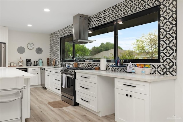 kitchen with island exhaust hood, appliances with stainless steel finishes, light hardwood / wood-style floors, and white cabinetry