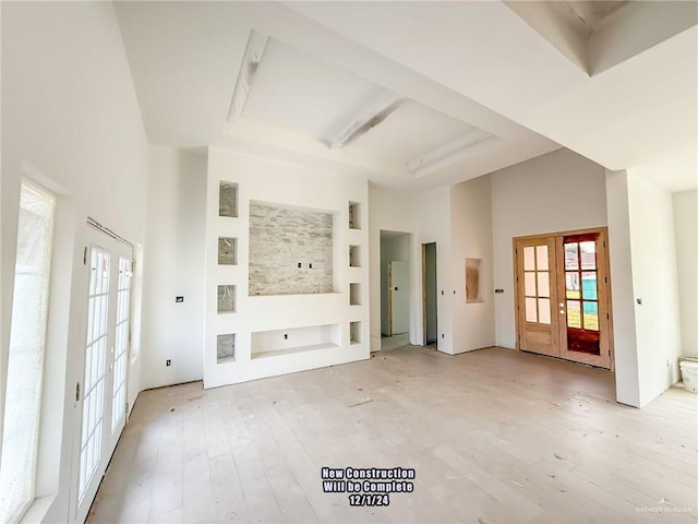 unfurnished living room with french doors, light wood-type flooring, and a high ceiling