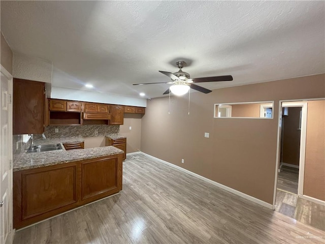 kitchen featuring a ceiling fan, a sink, baseboards, and light wood-type flooring