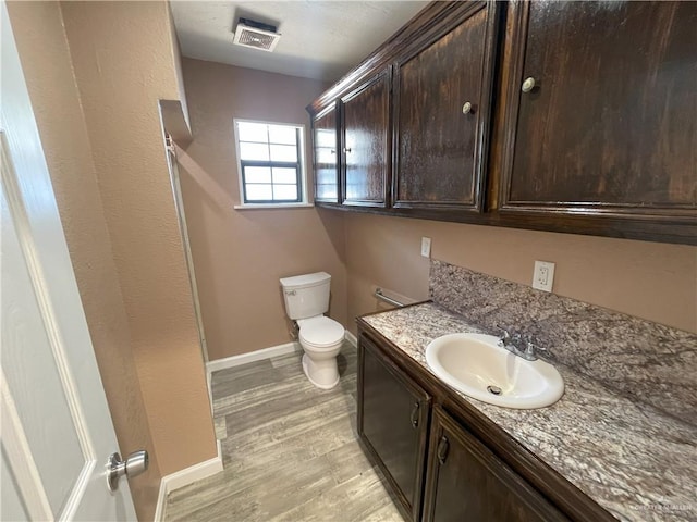 bathroom featuring vanity, toilet, visible vents, baseboards, and wood finished floors