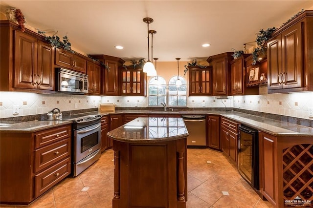 kitchen with sink, hanging light fixtures, appliances with stainless steel finishes, a kitchen island, and beverage cooler