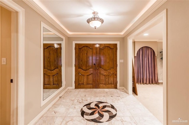 foyer with ornamental molding and a raised ceiling