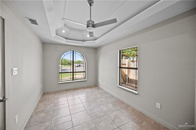 spare room featuring visible vents, a ceiling fan, baseboards, and a raised ceiling