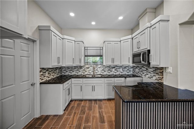 kitchen with decorative backsplash, dark wood-style flooring, stainless steel microwave, a sink, and dark stone countertops