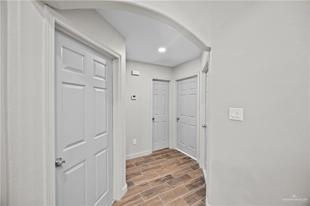 corridor featuring baseboards, recessed lighting, arched walkways, and wood finished floors