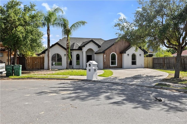 view of front facade featuring fence, stucco siding, concrete driveway, and roof with shingles
