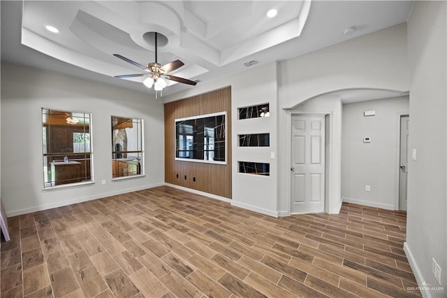 unfurnished living room featuring arched walkways, baseboards, a ceiling fan, and wood finished floors