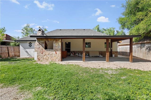 back of house featuring fence, stone siding, a patio, a shingled roof, and a lawn
