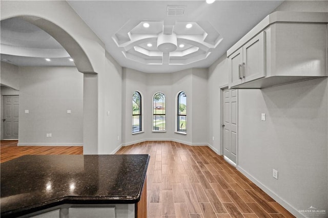 unfurnished dining area with baseboards, recessed lighting, a raised ceiling, arched walkways, and light wood-style flooring